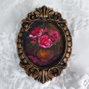May include: Oval-shaped oil painting of pink roses in a vase, set in a decorative gold-colored frame. The artwork features a dark background and a textured, impressionistic style, evoking a classic aesthetic.