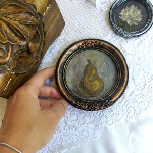 Puede incluir: Una peque&ntilde;a pintura enmarcada de una pera con un marco marr&oacute;n y dorado. La pera est&aacute; pintada en un estilo realista con una gama de colores amarillos y verdes.