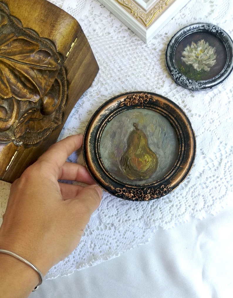 Puede incluir: Una peque&ntilde;a pintura enmarcada de una pera con un marco marr&oacute;n y dorado. La pera est&aacute; pintada en un estilo realista con una gama de colores amarillos y verdes.