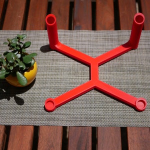 May include: A red plastic stand with four circular openings, designed to hold items like candles or small plants.