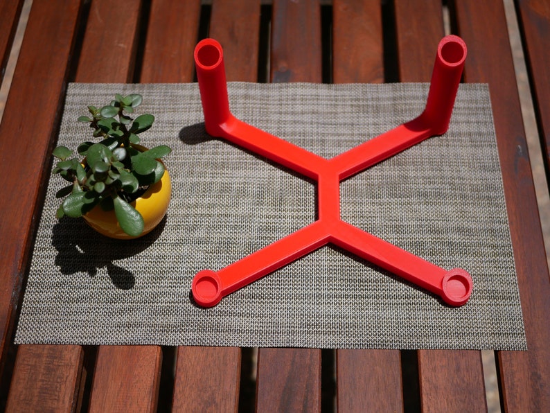 May include: A red plastic stand with four circular openings, designed to hold items like candles or small plants.