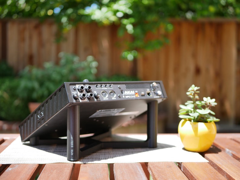 May include: Black audio interface with multiple ports and connections, sitting on a wooden table with a small yellow planter with a green succulent plant.