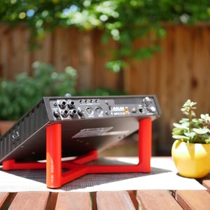 May include: A black music production interface with a red stand, the interface has a label that says "AKAI LPK25". The interface is sitting on a wooden table with a small yellow pot with a green plant.