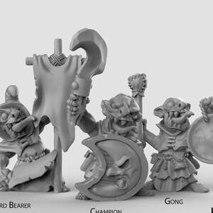 Pode incluir: Três miniaturas de plástico cinzento de goblins, cada uma com uma arma ou acessório diferente. O goblin à esquerda segura uma bandeira, o goblin do meio segura um escudo com um desenho de lua crescente, e o goblin à direita segura um gongo.