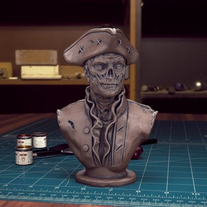 May include: A brown painted bust of a zombie pirate wearing a tricorn hat. The bust is on a wooden base and is sitting on a green cutting mat.