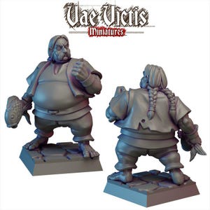 Puede incluir: Dos figuras en miniatura grises de un personaje corpulento sosteniendo un pez. El personaje lleva una túnica y pantalones, y tiene un peinado trenzado. Las figuras están sobre una base de piedra. El texto "Vae Victis Miniatures" está en la parte superior.