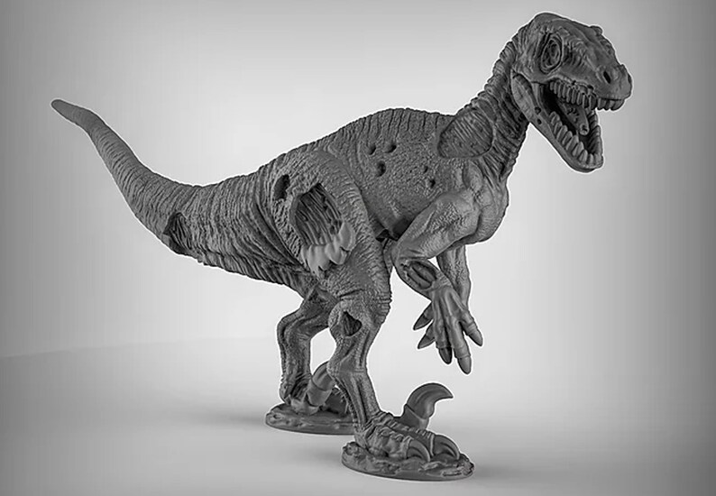 May include: A gray, detailed, plastic miniature of a velociraptor dinosaur with a damaged body and open mouth. The dinosaur is standing on a base with a textured surface.