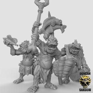 Pode incluir: Três figuras em miniatura pintadas de cinza que representam criaturas semelhantes a sapos segurando um cajado, uma concha e uma concha grande. As criaturas usam sungas e têm olhos grandes e expressivos.