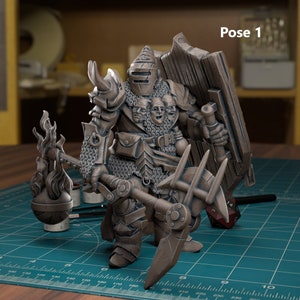 May include: A miniature figurine of a warrior with multiple faces, wearing armor and holding a flaming weapon and a shield. The figurine is painted in a bronze color and is posed in a fighting stance. The figurine is on a green mat with a ruler and a dice.