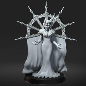 Puede incluir: Figura gris de una mujer regia con cuello ribeteado de piel y un vestido largo. Tiene una corona y una gran estructura ornamental en forma de halo detrás de ella. La figura está sobre una base negra, con los brazos extendidos.
