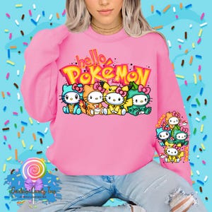May include: Pink sweatshirt with the text "hello Pokemon" in a colorful graphic font. The graphic features a row of cartoon characters with Hello Kitty-like faces wearing Pokemon hats.