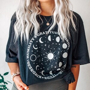 May include: Black oversized t-shirt with a white circle graphic featuring a sun, moon phases, and stars. The text around the circle reads "Gratitude, Kindness, Humility,  Kindness, Gratitude".