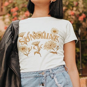 May include: A white t-shirt with a brown graphic that says "Sunshine state of mind" with yellow flowers around the text.