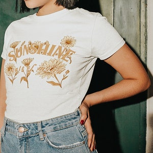 May include: White t-shirt with a graphic print of yellow flowers and the text "Sunshine state of mind".