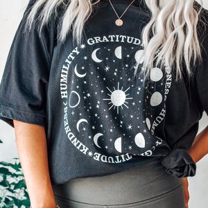 May include: Black oversized t-shirt with a graphic of a sun and moon phases with the words "Gratitude, Kindness, Humility" around the graphic.