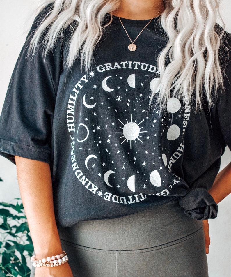 May include: Black oversized t-shirt with a graphic of a sun and moon phases with the words "Gratitude, Kindness, Humility" around the graphic.
