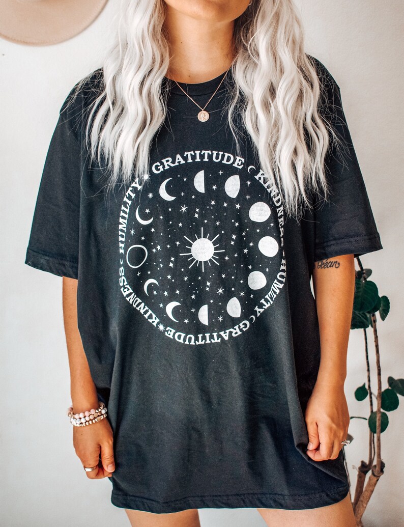 May include: Black oversized t-shirt with a graphic print of a circle with moons, stars, and a sun in the center. The text around the circle reads "Gratitude, Kindness, Humility".