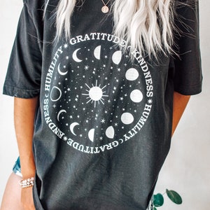 May include: Black oversized t-shirt with a white graphic of a sun and moon phases with the words "Gratitude, Kindness, Humility" repeated around the circle.