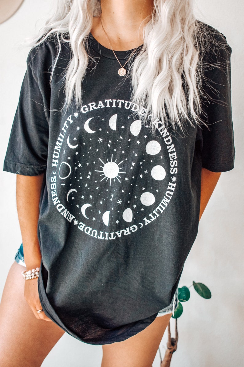 May include: Black oversized t-shirt with a white graphic of a sun and moon phases with the words "Gratitude, Kindness, Humility" repeated around the circle.
