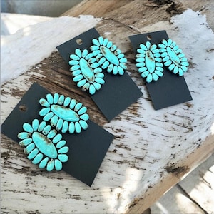 May include: A pair of turquoise blue earrings with a flower-like design. The earrings are displayed on black cards.