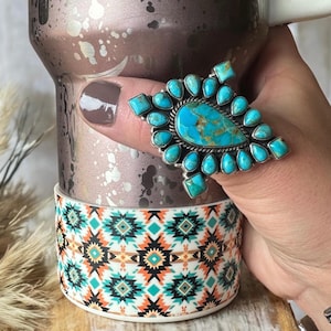 May include: A large turquoise ring with a silver setting. The ring features a large, teardrop-shaped turquoise stone surrounded by smaller turquoise stones.