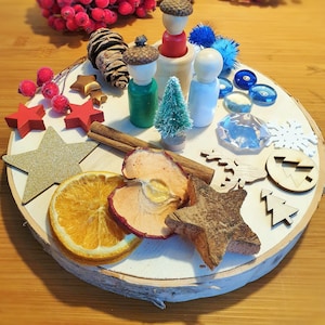 Könnte beinhalten: Ein Holztablett mit einer Vielzahl von natürlichen und dekorativen Gegenständen, darunter ein kleiner Kiefernbaum, Zimtstangen, getrocknete Apfelscheiben, ein sternförmiges Holzstück und drei Holzfiguren. Das Tablett ist mit einer Schneeflocke, einem Holzstern und einem Holzbaum verziert.