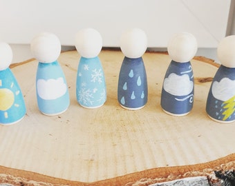 May include: Set of six wooden peg dolls painted to represent different weather conditions. The dolls are painted in shades of blue, gray, and yellow, with details like a sun, clouds, snowflakes, raindrops, and lightning.