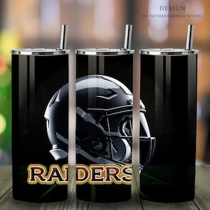 Könnte beinhalten: Ein schwarzer und silberner Becher mit einem Footballhelm-Motiv und dem Wort "RAIDERS" in goldenen Buchstaben. Der Becher hat einen schwarz-weiß gestreiften Hintergrund.
