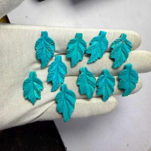 May include: Ten individual turquoise-coloured stone carvings shaped like leaves. Each piece features detailed etched veins and a pointed tip. The carvings are arranged in a loose cluster, displaying a consistent bright blue-green hue and smooth surface texture across all ten items.