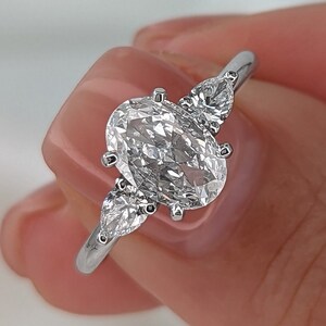 May include: A silver ring with a large oval-shaped diamond and two smaller pear-shaped diamonds on either side.