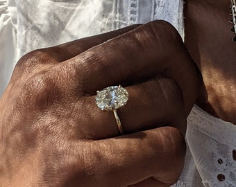Pode incluir: Um close-up de uma mão usando um anel de ouro com um grande diamante oval. O anel é definido em uma banda simples.
