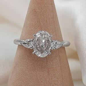 May include: A silver ring with an oval-shaped diamond and two smaller diamonds on either side. The ring is displayed on a wooden ring holder.