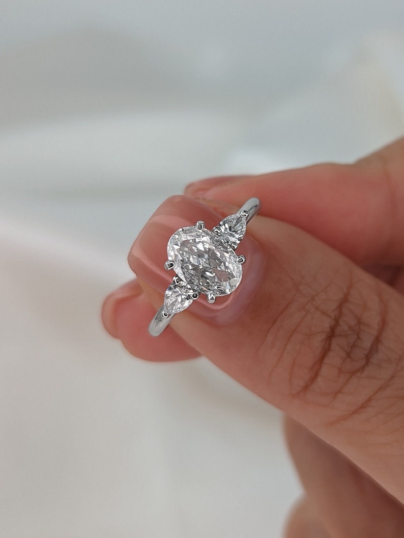 May include: A silver ring with a large oval-shaped diamond and two smaller pear-shaped diamonds on either side.
