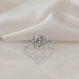 May include: A silver ring with a large oval-shaped diamond and two smaller diamonds on either side.