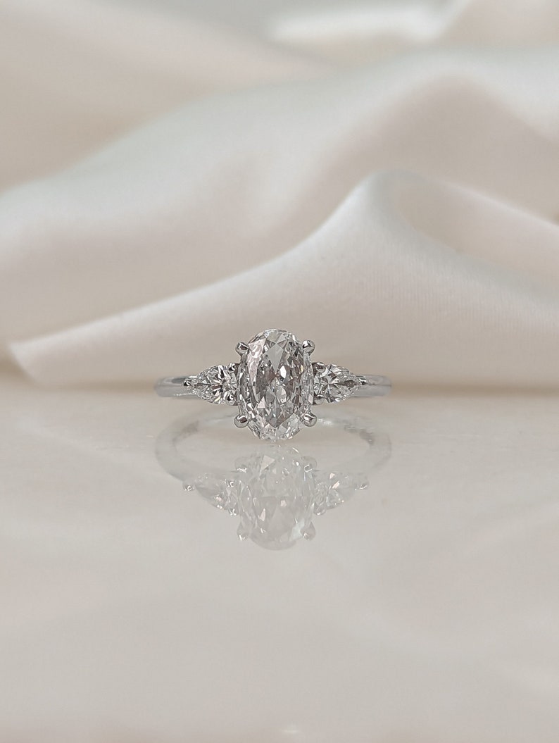 May include: A silver ring with a large oval-shaped diamond and two smaller diamonds on either side.