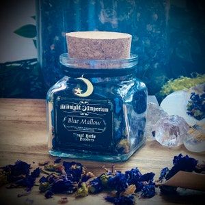 Könnte beinhalten: Ein Glasgefäß mit einem Korkverschluss, gefüllt mit getrockneten blauen Malvenblüten. Das Gefäß hat ein schwarzes Etikett mit dem Text "Midnight Imperium Blue Mallow Finest Herbs & Powders".