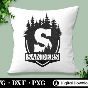 Puede incluir: Una almohada blanca con una silueta negra de un bosque y la letra "S" dentro de un escudo. El texto "SANDERS" est&aacute; debajo del escudo.