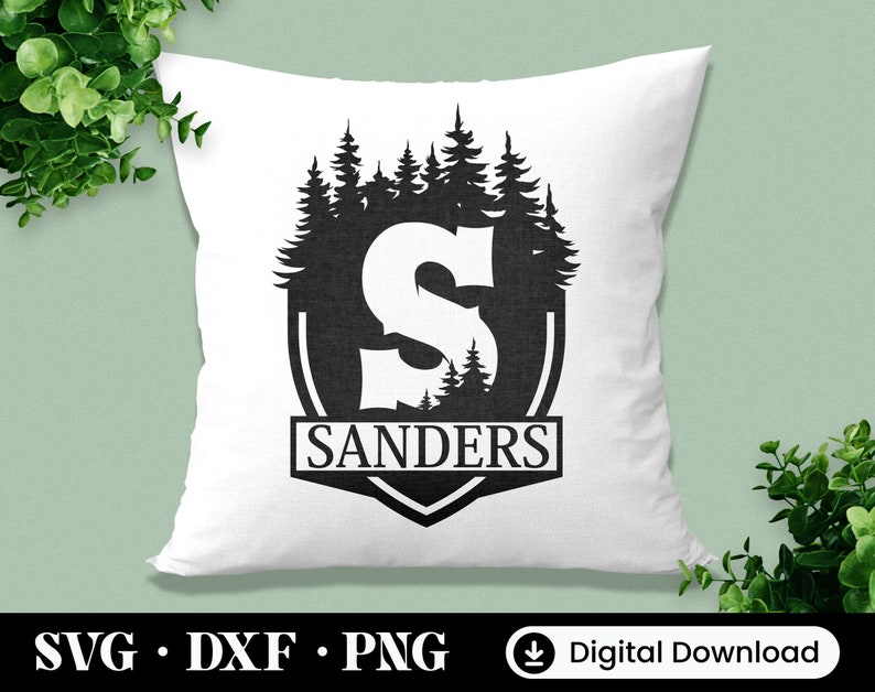 Puede incluir: Una almohada blanca con una silueta negra de un bosque y la letra "S" dentro de un escudo. El texto "SANDERS" est&aacute; debajo del escudo.