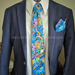 May include: A navy blue suit with a white collared shirt, a blue tie, and a matching pocket square. The tie and pocket square feature a vibrant underwater scene with colorful fish, coral, and dolphins.