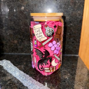May include: A glass jar with a bamboo lid, decorated with a pink and black dragon, a sword, a potion bottle, and the text "I will not die today".