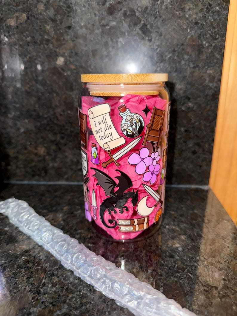 May include: A glass jar with a bamboo lid, decorated with a pink and black dragon, a sword, a potion bottle, and the text "I will not die today".