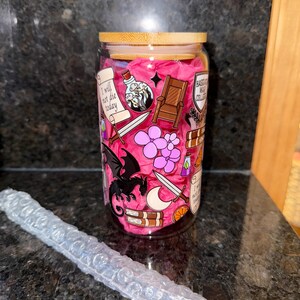 May include: A clear glass tumbler with a pink background and various illustrations, including a dragon, a sword, a crown, a potion bottle, and a book. The tumbler has a bamboo lid and the text "I will not die today" and "Based God Collector" are visible on the tumbler.
