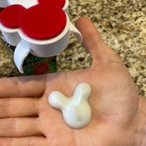 May include: A white hand cream in the shape of Mickey Mouse's head. The cream is a light white color and has a smooth texture.