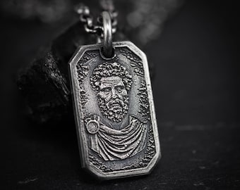 May include: A silver-colored rectangular pendant necklace featuring a detailed engraved portrait of a man with a beard and curly hair. The pendant is attached to a silver chain, with a dark background.