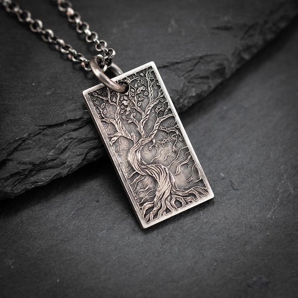 May include: A silver rectangular pendant with a detailed tree of life design. The pendant hangs from a silver chain. The tree features a twisted trunk, branches, and leaves. The pendant is approximately 3.8 cm long.