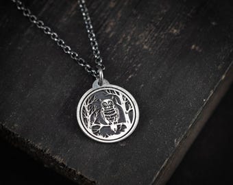 May include: A silver-colored pendant necklace featuring a detailed owl design. The circular pendant showcases an owl perched on a branch within a forest scene. The necklace has a delicate chain, and the pendant is approximately 1 inch in diameter.