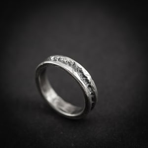 May include: A silver ring with a textured, carved design. The ring features a detailed pattern around the band. The metal has a slightly aged appearance, giving it a vintage feel. The ring's circumference is approximately 2 cm.