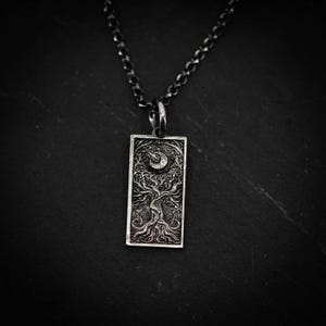 May include: A silver-toned pendant necklace featuring a rectangular pendant with a detailed tree design. The tree is beneath a crescent moon and stars. The chain is a dark, oxidized silver color. The pendant is approximately 1 inch in length.
