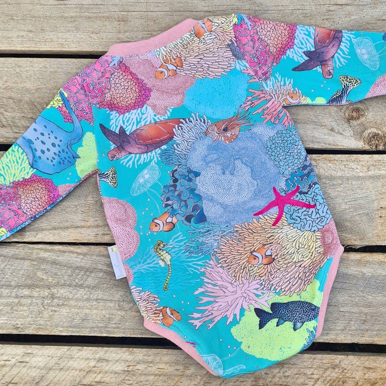 May include: A turquoise long-sleeved baby onesie with a coral reef print featuring colorful fish, sea turtles, and coral.