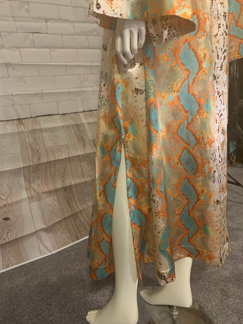 May include: A long, flowing dress with a snakeskin print in shades of orange, blue, and white. The dress has a side slit and a fitted bodice.